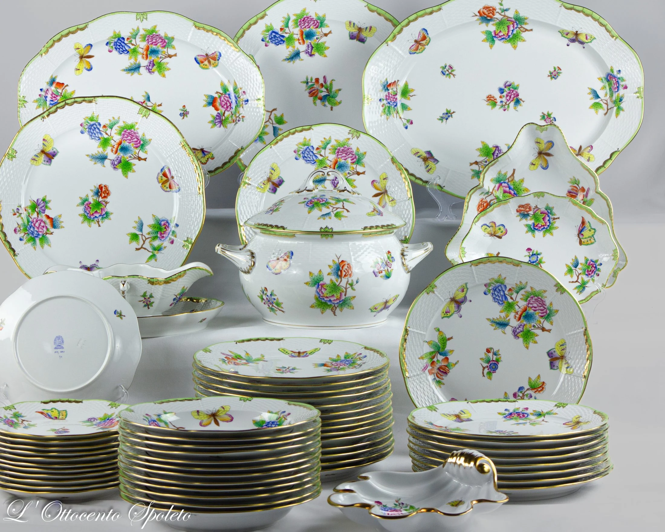 Vista d’insieme del servizio da pranzo Herend Queen Victoria di 56 pezzi, con piatti, zuppiera, salsiera e complementi decorati con fiori e farfalle e bordi verdi e dorati.