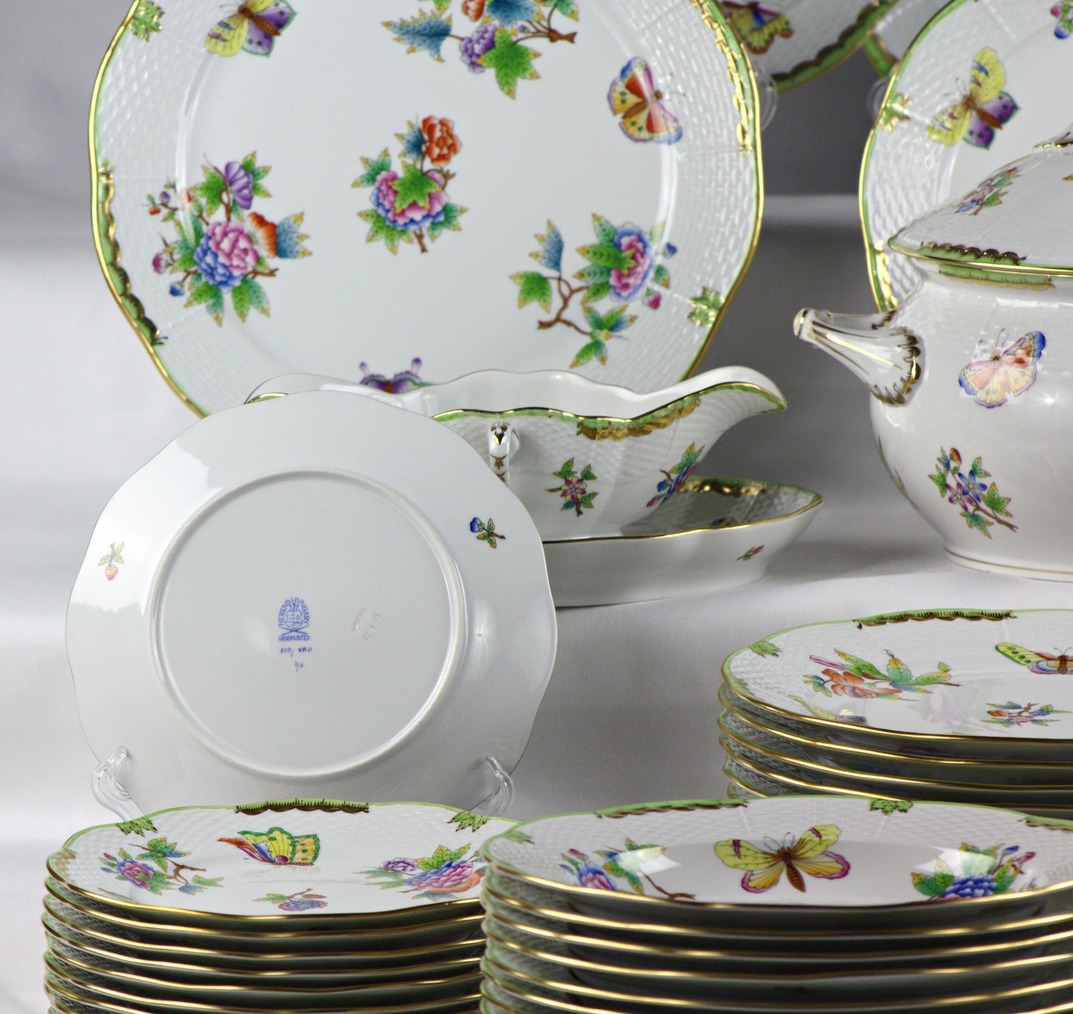 Fondo di un piatto e salsiera sullo sfondo del servizio Herend Queen Victoria, con decoro di fiori e farfalle.