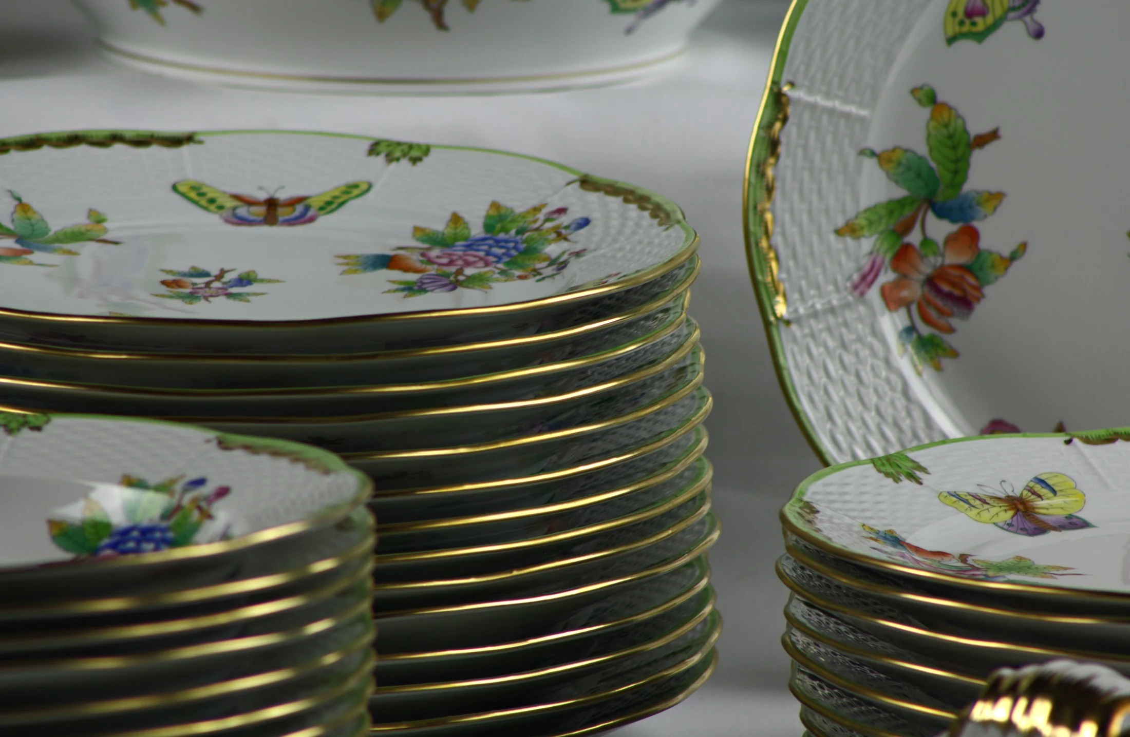 Piatti impilati e dettaglio dei bordi dorati del servizio Herend Queen Victoria, con decoro di fiori e farfalle.